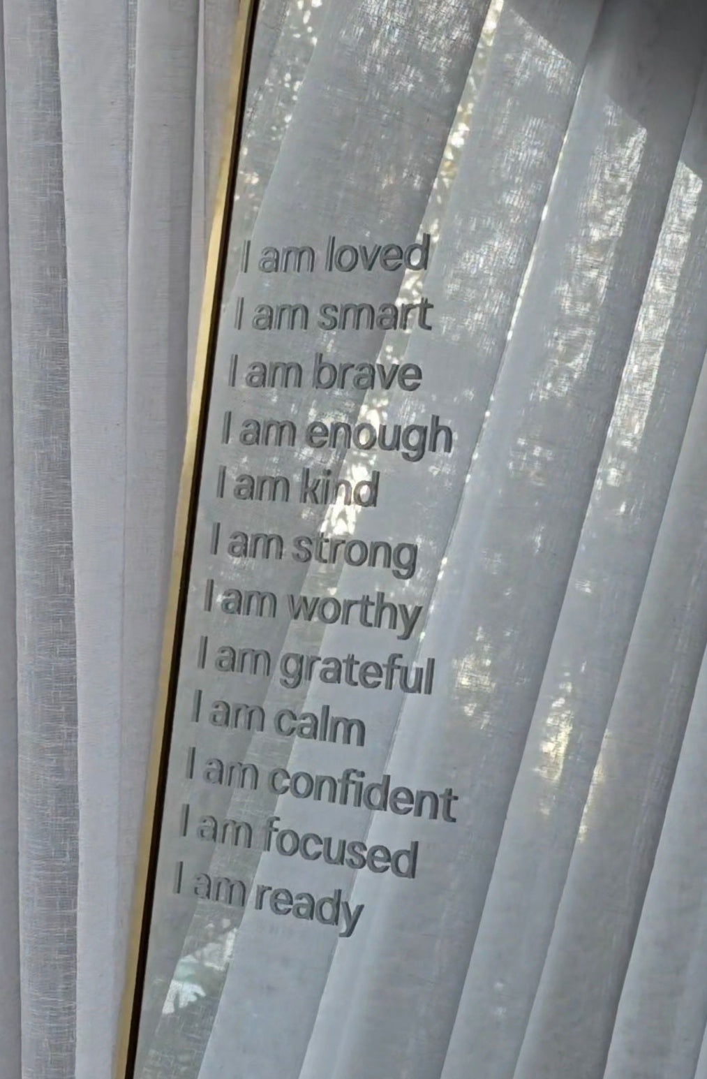White sheer curtains next to a mirror with printed positive self-affirmations in white text