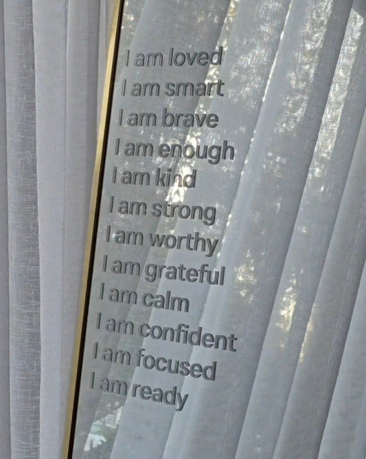 White sheer curtains next to a mirror with printed positive self-affirmations in white text